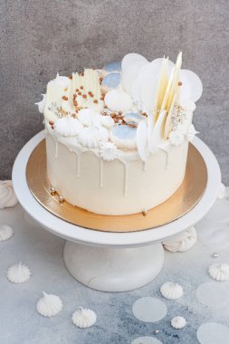 Çikolata süslemeli zarif beyaz düğün pastası, gri arka planda kremalar ve badem kurabiyeleri..