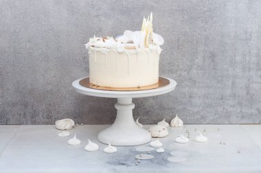 Çikolata süslemeli zarif beyaz düğün pastası, gri arka planda kremalar ve badem kurabiyeleri..