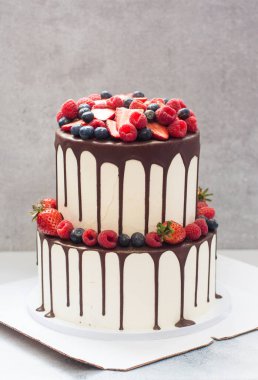 Taze böğürtlen ve erimiş çikolatayla süslenmiş üç katlı beyaz bir düğün pastası.