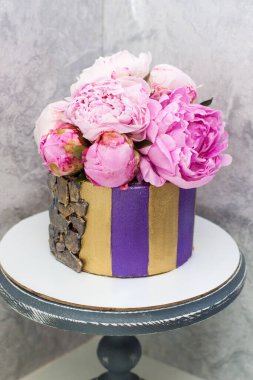 Modern, zarif menekşe ve taze şakayık çiçekleriyle süslenmiş altın çizgili pasta. Gri arkaplan