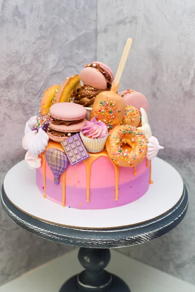 Bolo de aniversário rosa e laranja decorado com macaroons, merengues, donuts, cones de waffle, pops de bolo e barras de chocolate . — Fotografia de Stock