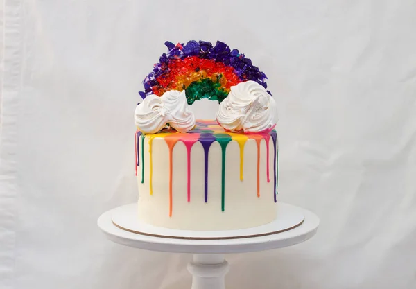 LGBT rainbow cake with melted chocolate and caramel rainbow on white cakestand. Plain white background, copy space.