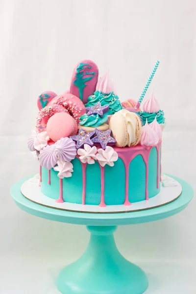 Pink and turquoise cake decorated with macaroons, cupcakes, cake pops, meringues, popsicles and melted chocolate. — Stock Photo, Image