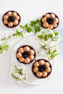Tuzlu karamelli çikolatalı tart ve taze böğürtlen. Arka planda kiraz çiçekleri. Boşluğu kopyala.