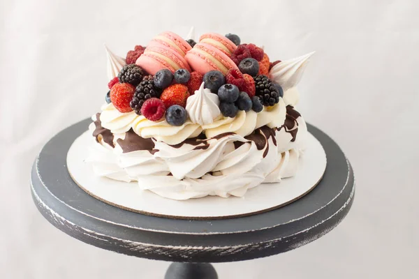 Pavlova cake with whipped cream, raspberry, blueberry, blackberry and french macaroons. Copy space, plain grey background.