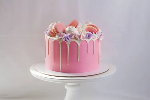 柔和的粉红蛋糕 用融化的白巧克力 金银花 蛋白糖 蛋糕和糖果装饰在白色的蛋糕架上 朴素的背景 — 图库照片
