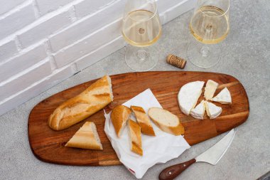 İki kadeh beyaz şarap, Camemebert peynirli bıçak ve tahtanın üzerinde baget. Beyaz tuğla arkaplan.