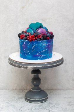 Taze böğürtlen, badem kurabiyesi ve şekerle süslenmiş kır pastası üzerine uzay mavisi pastası. Gri arkaplan