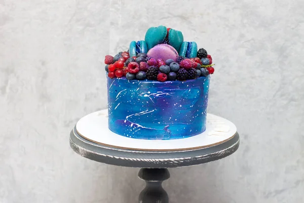 Taze böğürtlen, badem kurabiyesi ve şekerle süslenmiş kır pastası üzerine uzay mavisi pastası. Gri arkaplan