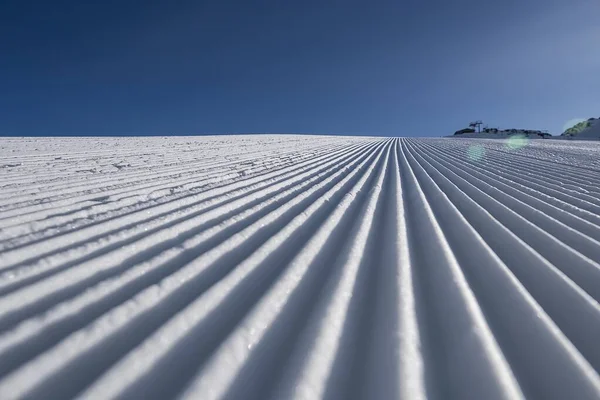 Snow samet zblízka na sjezdovce na pozadí zasněžených vrcholků hor. Připravená lyžařská a snowboardová dráha se stopou sněžného pěšáka na sněhu. Rakousko, Pitztal Hoch Zeiger. — Stock fotografie