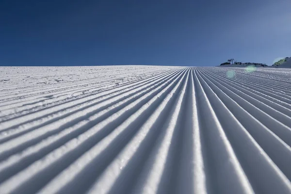 Sneeuwfluweel close-up op de skipiste op de achtergrond van besneeuwde bergtoppen. Voorbereid ski- en snowboardparcours met sporen van sneeuwruimer op sneeuw. Oostenrijk, Pitztal Hoch Zeiger. — Stockfoto