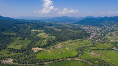 Karpat Dağları 'nın havadan görünüşü. Geometrik desenli doğal arka plan - tarlaların bej ve kırmızı dikdörtgenleri ve çatılar ve yollar ve ağaçlar. Zakarpattia, Ukrayna.