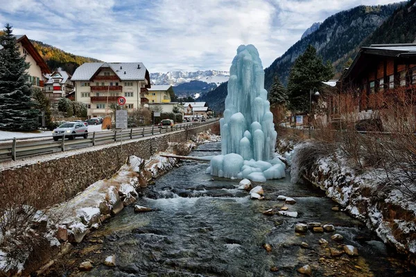 La fontaine gelée d'Ortisei, village italien des Dolomites Alpes en Italie : maisons, bâtiments et église paroissiale avec clocher au milieu des sommets enneigés et des conifères , — Photo