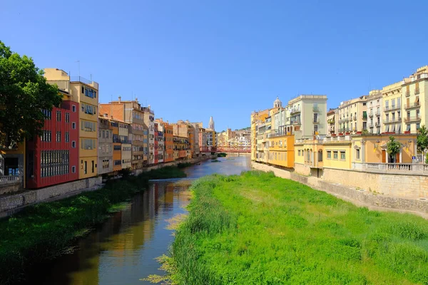 Kleurrijke gele en oranje huizen en Eiffel Bridge, oude vis kraampjes, weerspiegeld in water rivier Onyar, in Girona, Catalonië, Spanje. Kerk van Sant Feliu op achtergrond. — Stockfoto