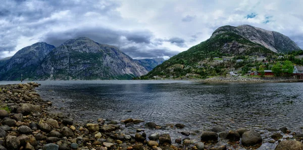 Une chaîne infinie de montagnes se reflétant dans une eau calme de l'Eidfjord. Les parties les plus hautes des montagnes sont partiellement recouvertes de neige. Temps nuageux. Paysage romantique — Photo