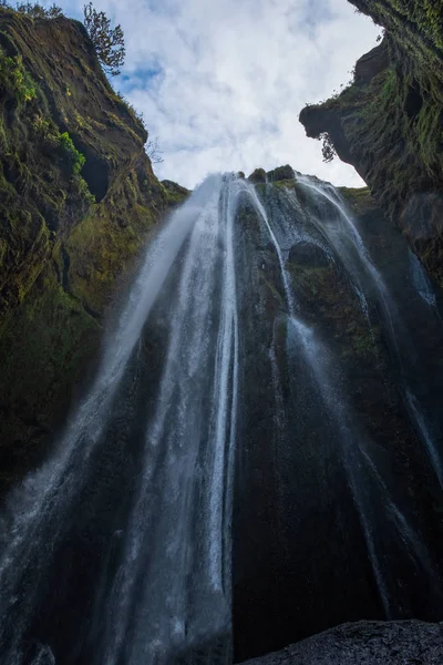 Gljufrafoss Gljufrabui şelalesi dağ geçidinde. Seljalandsfoss Şelalesi yakınlarındaki İzlanda turistik merkezi. Mavi ceketli bir adam taşın üzerinde duruyor ve düşen suyun akışına bakıyor.