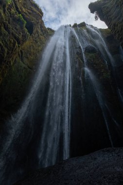 Gljufrafoss Gljufrabui şelalesi dağ geçidinde. Seljalandsfoss Şelalesi yakınlarındaki İzlanda turistik merkezi. Mavi ceketli bir adam taşın üzerinde duruyor ve düşen suyun akışına bakıyor.