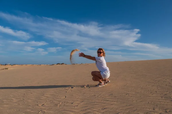 Young woman throws sand in dunes Corralejo, Fuerteventura. Canary Islands, Spain. October 2019