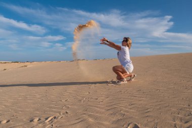 Genç kadın kum tepelerine kum atıyor Corralejo, Fuerteventura. Kanarya Adaları, İspanya. Ekim 2019
