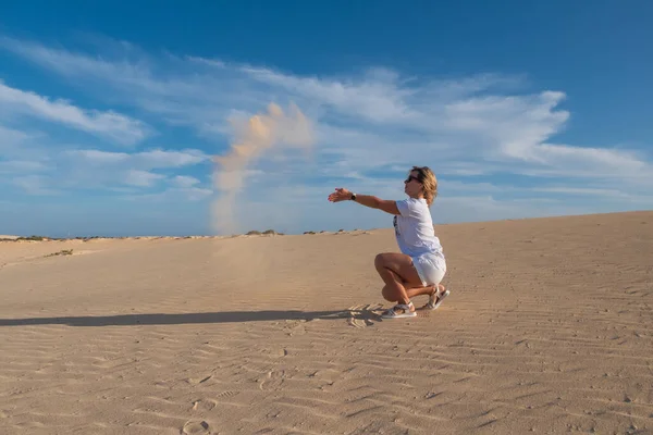 Young woman throws sand in dunes Corralejo, Fuerteventura. Canary Islands, Spain. October 2019