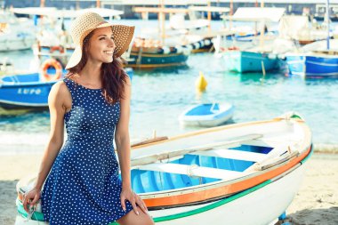 Güzel kadın teknede plajda otururken hasır şapkalı. Summe