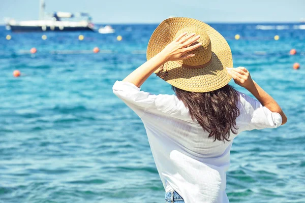 Frau mit Hut lehnt sich zurück und blickt aufs Meer — Stockfoto