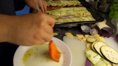 İnce dilimlere ayrılmış karışık sebzelerin hazırlanması, yağlanıp pişirilmesi için tavaya konması. Patlıcan, domates, patates, kabak ve kırmızı soğan.