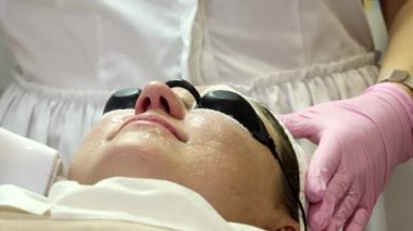 A woman is preparing for a laser rejuvenation procedure in the salon. A cosmetologist-dermatologist completes the photorejuvenation procedure. Shooting is from different angles