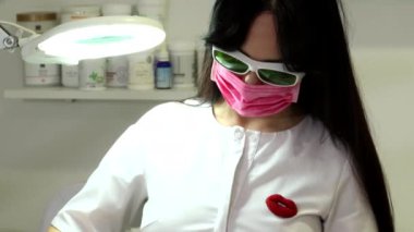 A woman is preparing for a laser rejuvenation procedure in the salon. A cosmetologist-dermatologist completes the photorejuvenation procedure. Shooting is from different angles