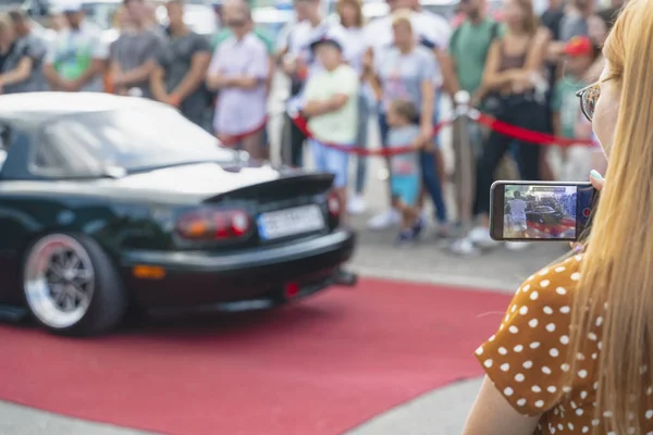 Kız cep telefonuyla yeni bir aracın fotoğrafını çekiyor. Ziyaretçi Ukrayna, Kiev 'de arabayı vurdu.
