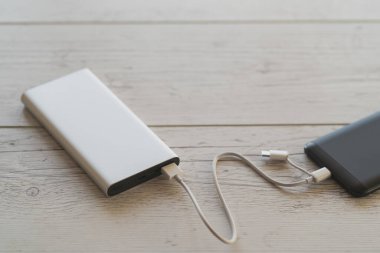Ahşap arka planda gümüş güç bankasından şarj olan akıllı telefon, renkli görüntü, yüksek açılı görüntü. Taşınabilir şarj aygıtı özellikle seyahat için üretken.