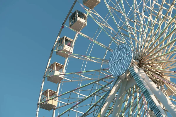 Большое колесо наблюдения вращается на голубом фоне неба. Люди ездят на Феррис Виле и веселятся в солнечный день. Низкий угол обзора, цветное изображение и макрос — стоковое фото