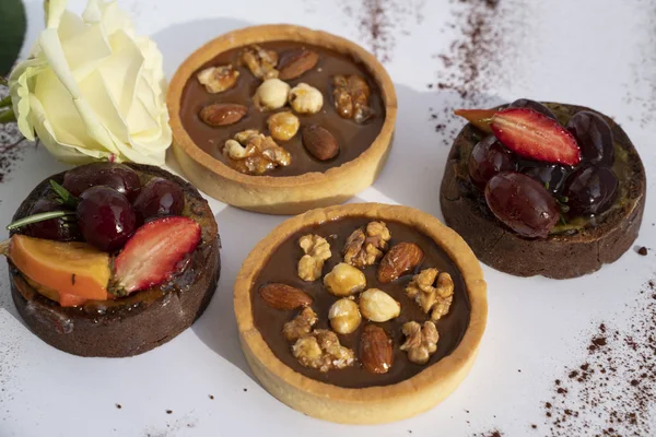 Arka planda beyaz gül olan meyveli ve fındıklı kekler, romantik tatlı. Yüksek açı görünümü, renk resmi ve makro.