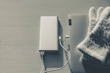 Kışın enerji bankasından kablosuz şarj olan dizüstü bilgisayar, şarj aleti, güneşli bir günde renkli arka planda. Taşınabilir şarj cihazı iş seyahatinde çok yardımcı olur. Üst görünüm.