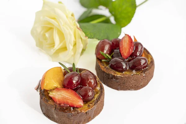 Beyaz arka planda meyveli ve meyveli iki lezzetli çikolatalı kek, izole edilmiş beyaz gül ve makro. Romantik tatlı..