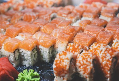 Philadelphia yeşil suşi ruloları taze somon, krem peynir, salatalık, avokado. Ginger ve Wasabi (Japon yaban turpu) ile suşi barında siyah seramik tepside servis edilir. Yatay görüntü, izole