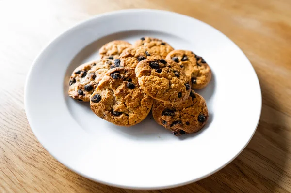 Choc chip cookies in a white plate on a wooden table. Close-up of homemade chocolate chip cookies. Traditional handmade chewy cookies with chocolate chunk. Basic drop cookies with chocolate morsels