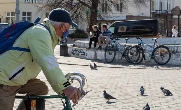Lutsk, Ukrayna - 20 Mayıs 2020: Coronavirüs salgınının ortasında aktif yaşam tarzı. Yüz maskesi ve eldiven takan yaşlı adam, şehirdeki bir karantina sırasında halka açık bir caddede bisiklet sürüyor.