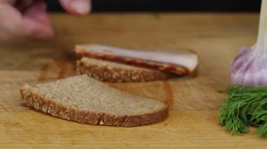 Kadın, gri ekmek ve pastırmalı sandviç yapar ve üzerine doğranmış bitkiler serper, yakın plan.