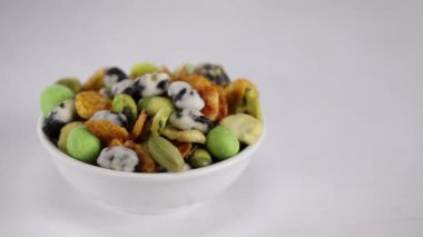 Fıstıklı, bezelyeli ve wasabi 'li Japon aperatifleri ön planda beyaz bir kasede, arka planda kadın elleri masaya diğer Japon aperatifleriyle birlikte iki fincan daha koydu.