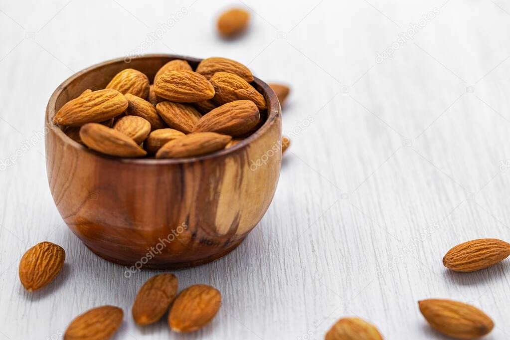Almond nuts in a brown wooden bowl on a white wooden background