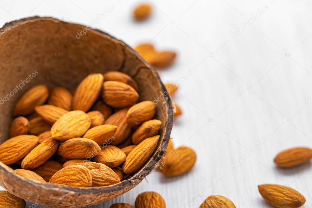 Almond nuts in half coconut shell on white wooden background