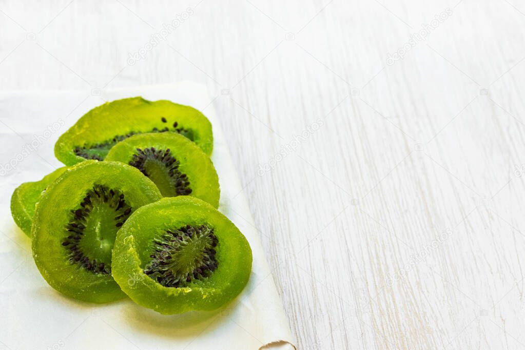 Slices of dried kiwi lie on food paper on a white wooden background