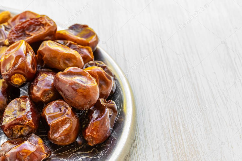 Dates lie on a silver tray on a white wooden background