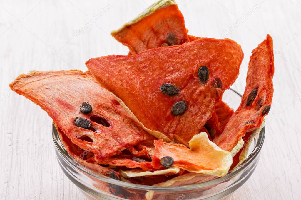 Dried watermelon chips lie in a glass transparent bowl