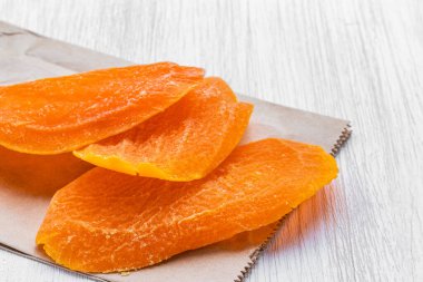 Gri bir kese kağıdında üç dilim kurutulmuş mango.