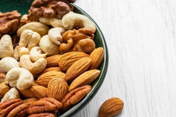 Beyaz ahşap bir yüzeyde yeşil bir tabakta çeşitli fındıklar.