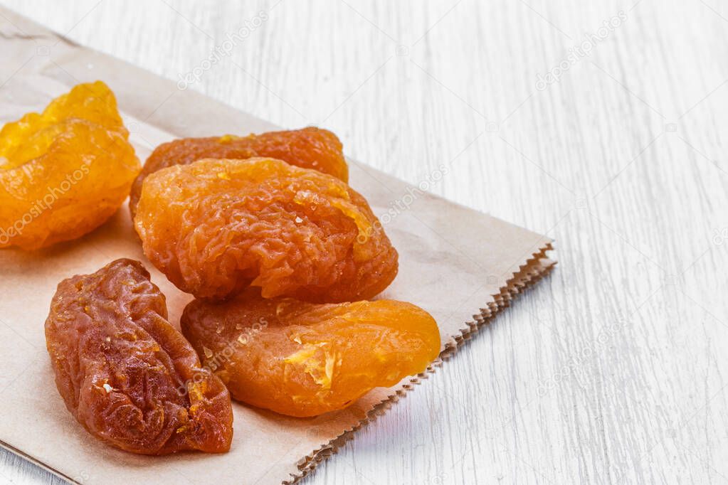 Halves of dried peach lie on a gray paper bag