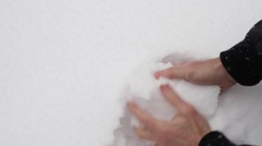 Adamın elleri düşen bir kar topunu yontuyor.