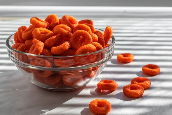 Paprika-style corn chips in the form of rings lie in a glass bowl